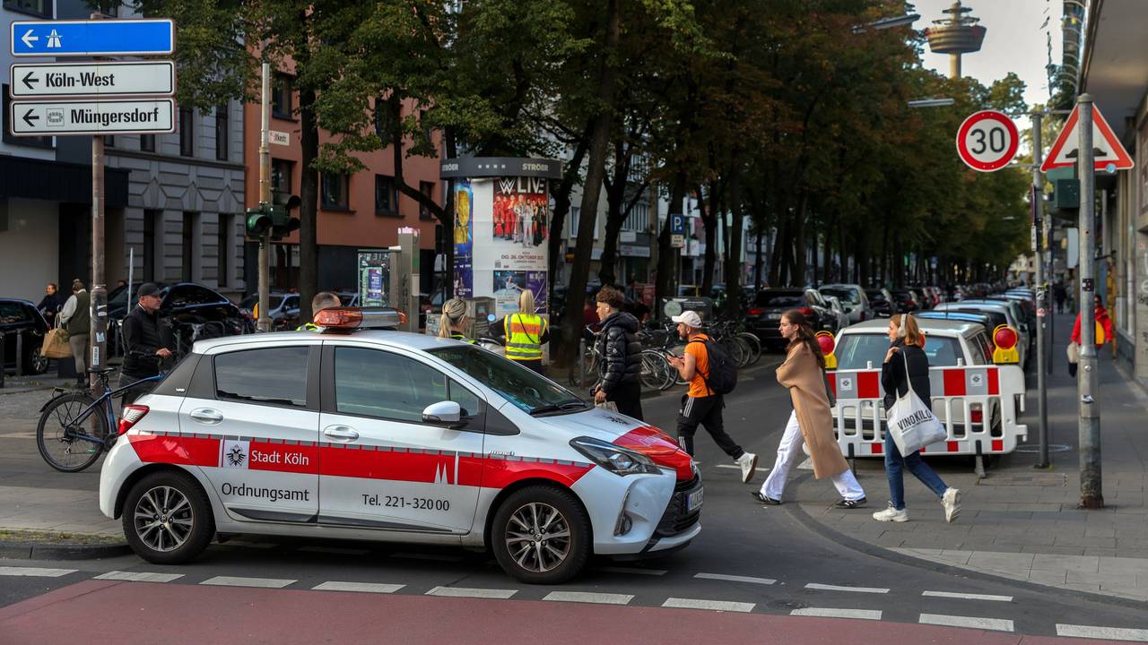 Ein Autos des Ordnungsamts sperrt eine Straße ab, Menschen gehen zu Fuß vorbei.