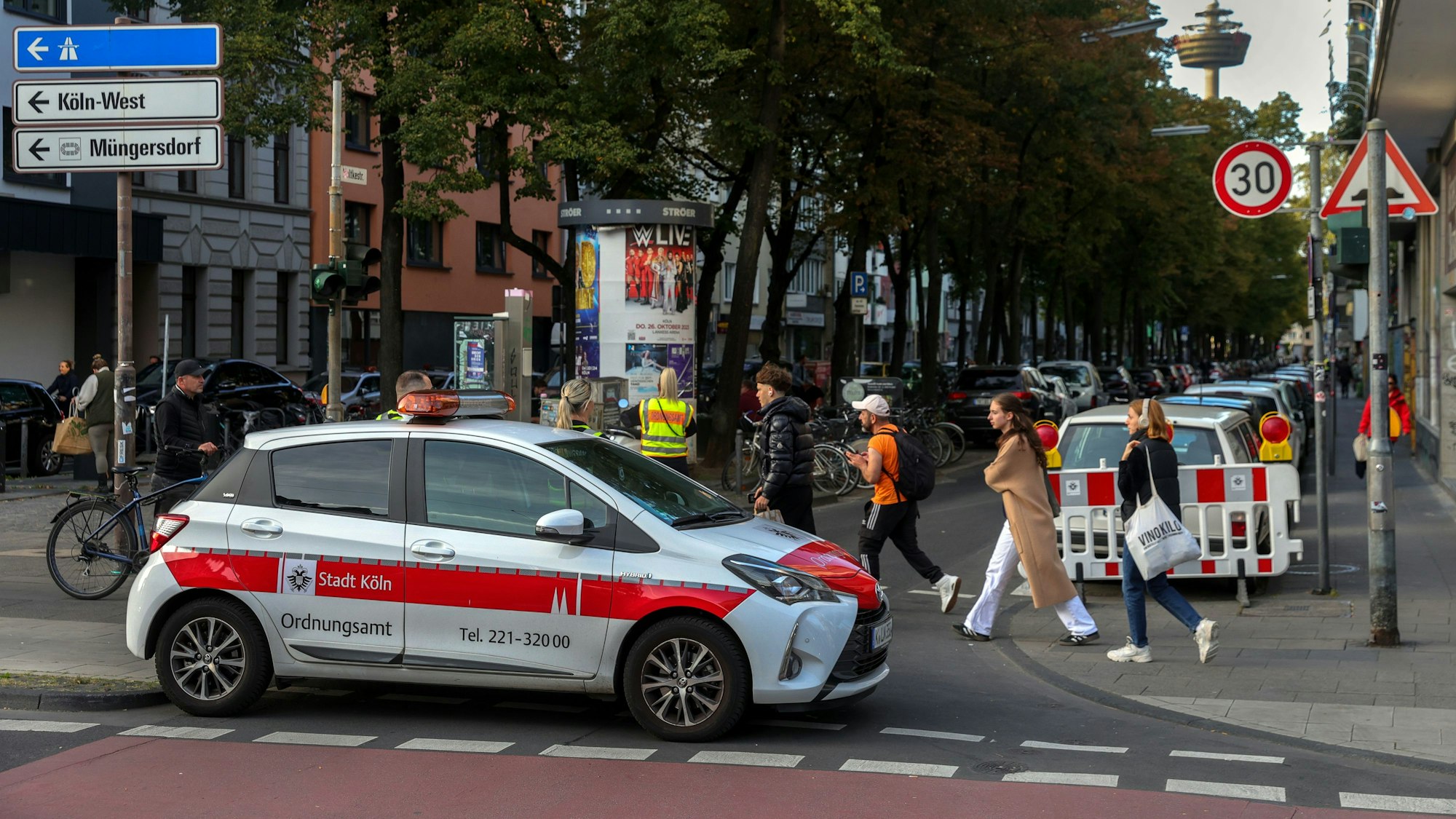Ein Autos des Ordnungsamts sperrt eine Straße ab, Menschen gehen zu Fuß vorbei.