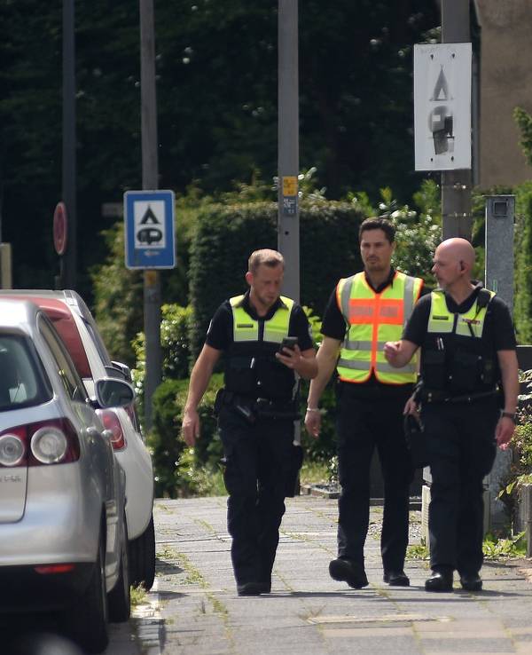 Drei männliche Mitarbeiter des Ordnungsdienst gehen an einer Straße entlang und informieren die Anwohner über eine Evakuierung.