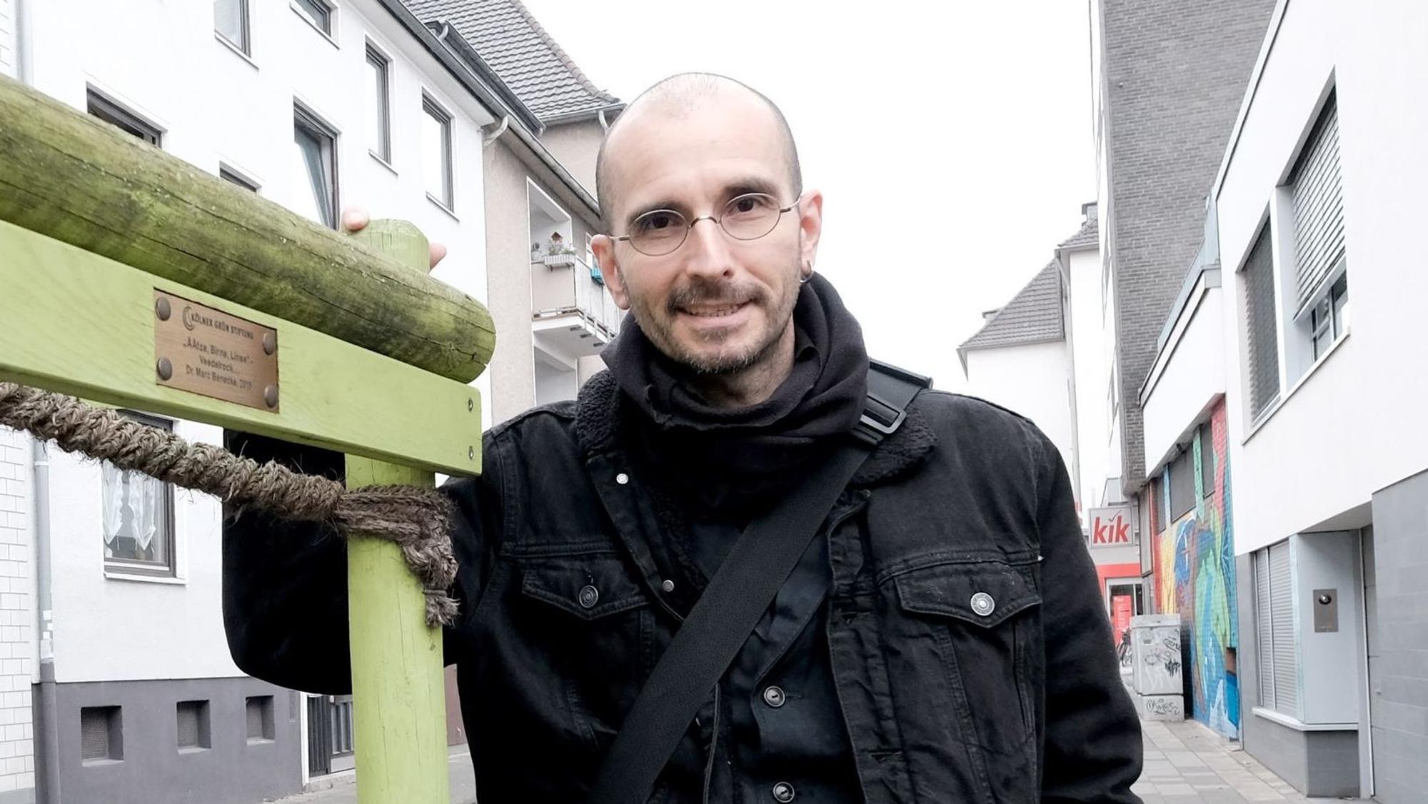 Dr. Mark Benecke steht an einem Baum in der Kölner Südstadt und lächelt in die Kamera.