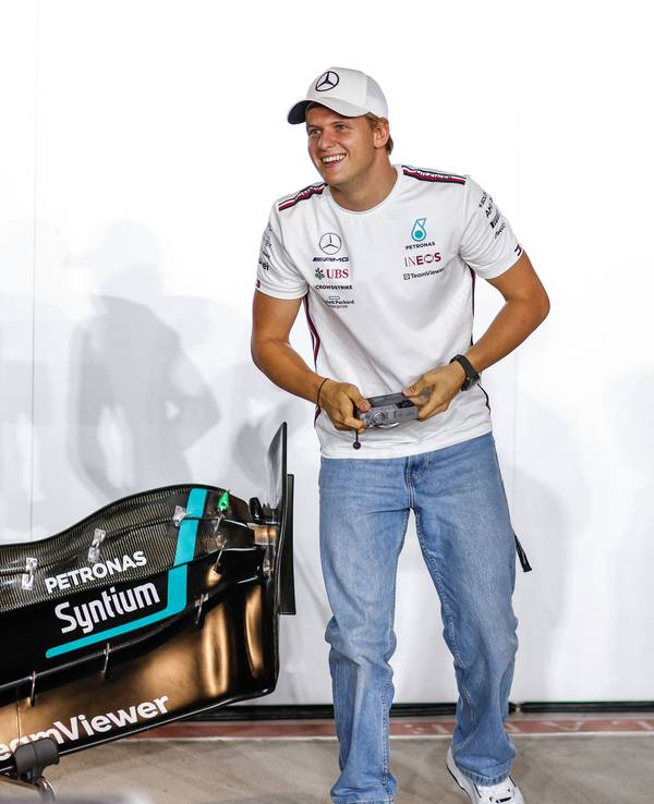 Mick Schumacher hält eine Kamera in der Hand und lacht dabei.