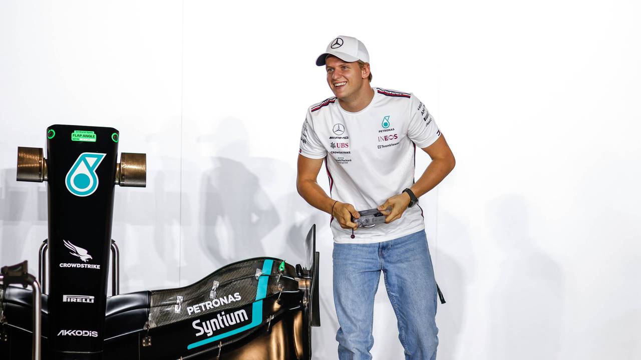 Mick Schumacher hält eine Kamera in der Hand und lacht dabei.