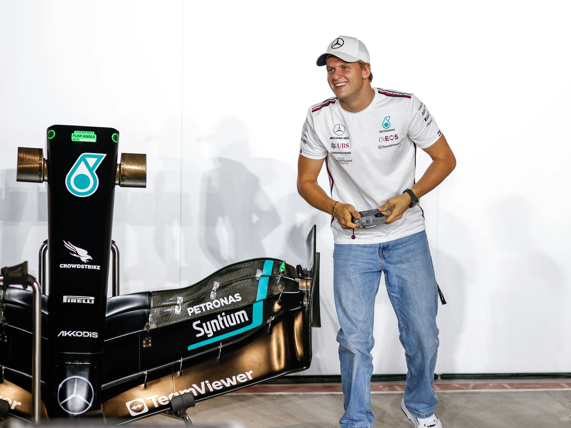 Mick Schumacher hält eine Kamera in der Hand und lacht dabei.