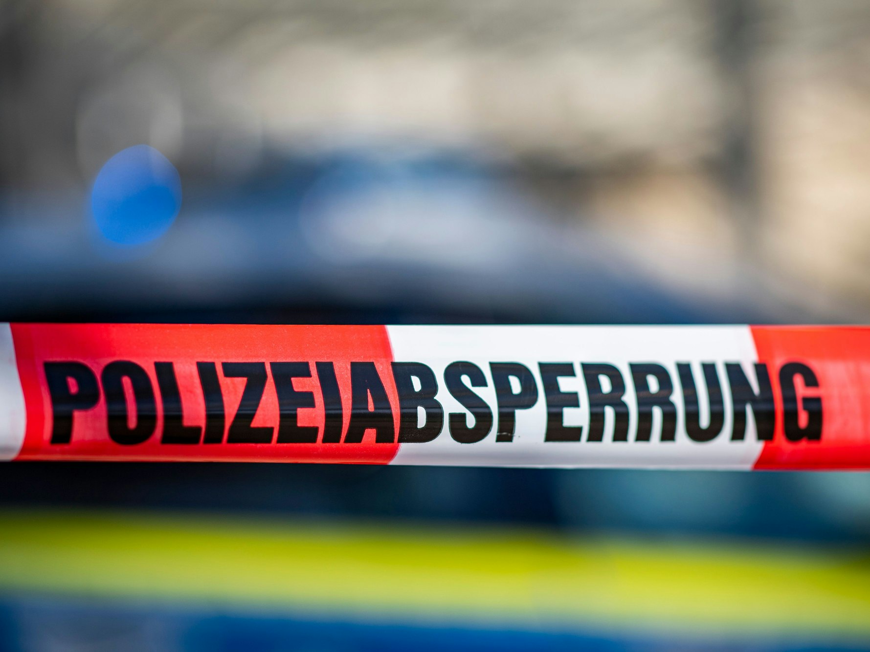 Ein Absperrband mit der Aufschrift „Polizeiabsperrung“ ist vor einem Polizeiwagen aufgespannt.