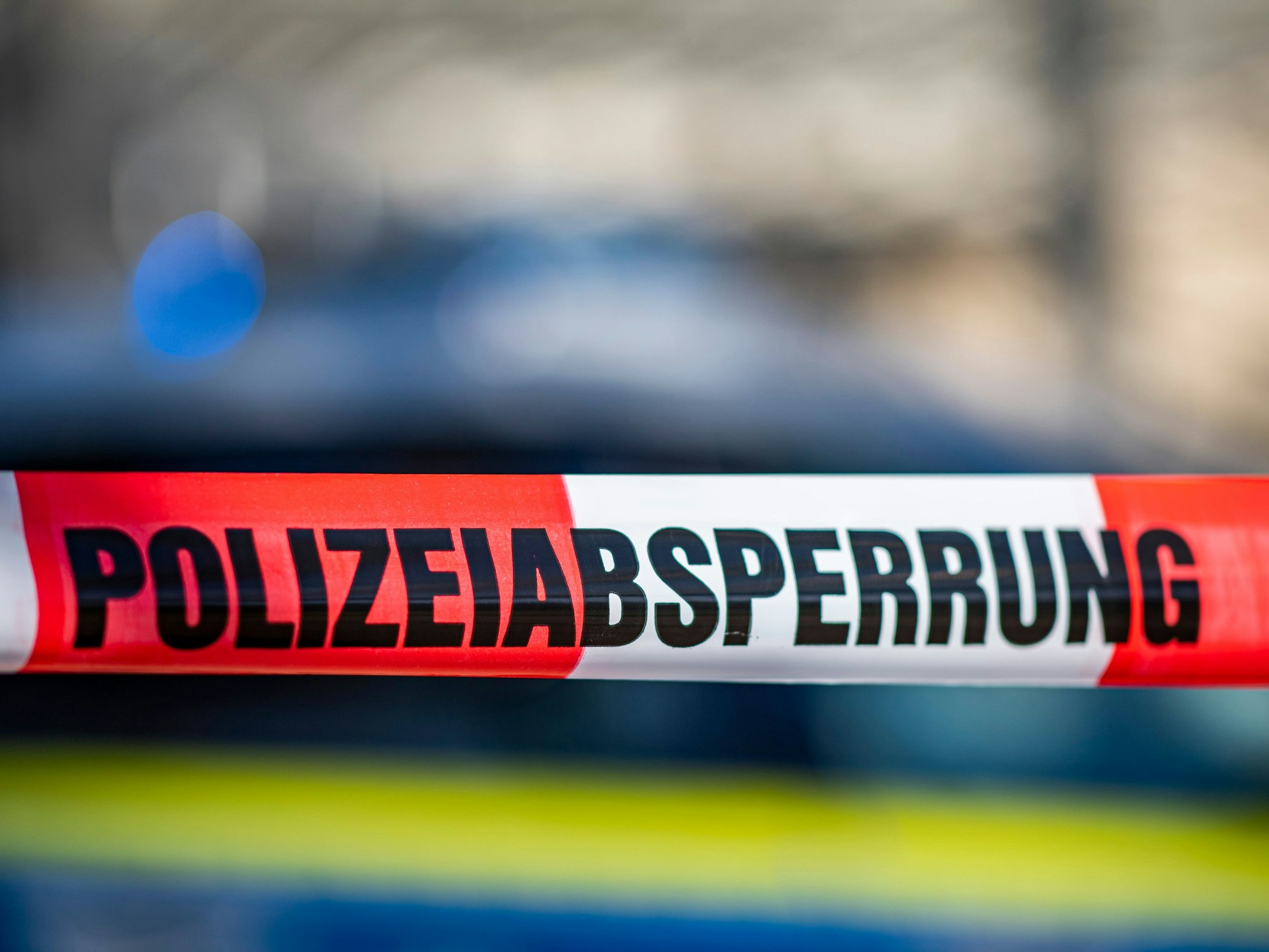 Ein Absperrband mit der Aufschrift „Polizeiabsperrung“ ist vor einem Polizeiwagen aufgespannt.
