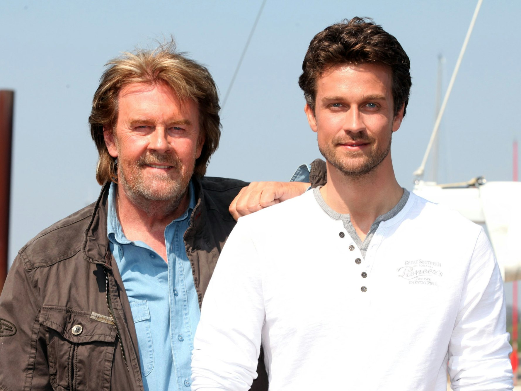 Schauspieler Wayne Carpendale und sein Vater, der Sänger Howard Carpendale, stehen im April 2011 in Hamburg unter blauem Himmel vor einem Hafen und lächeln in die Kamera.