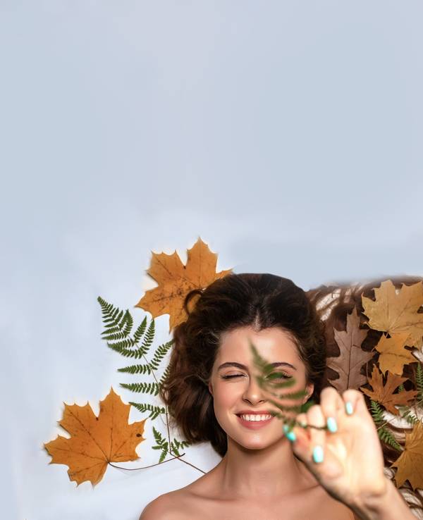 Eine junge Frau in herbstlicher Umgebung mit Blättern und Make-up in warmen, gedeckten Herbsttönen.