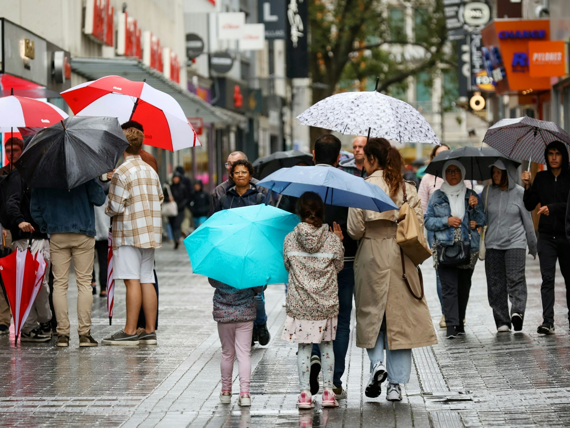 Menschen mit Regenschirmen laufen über die Fußgängerzone der Hohe Straße.