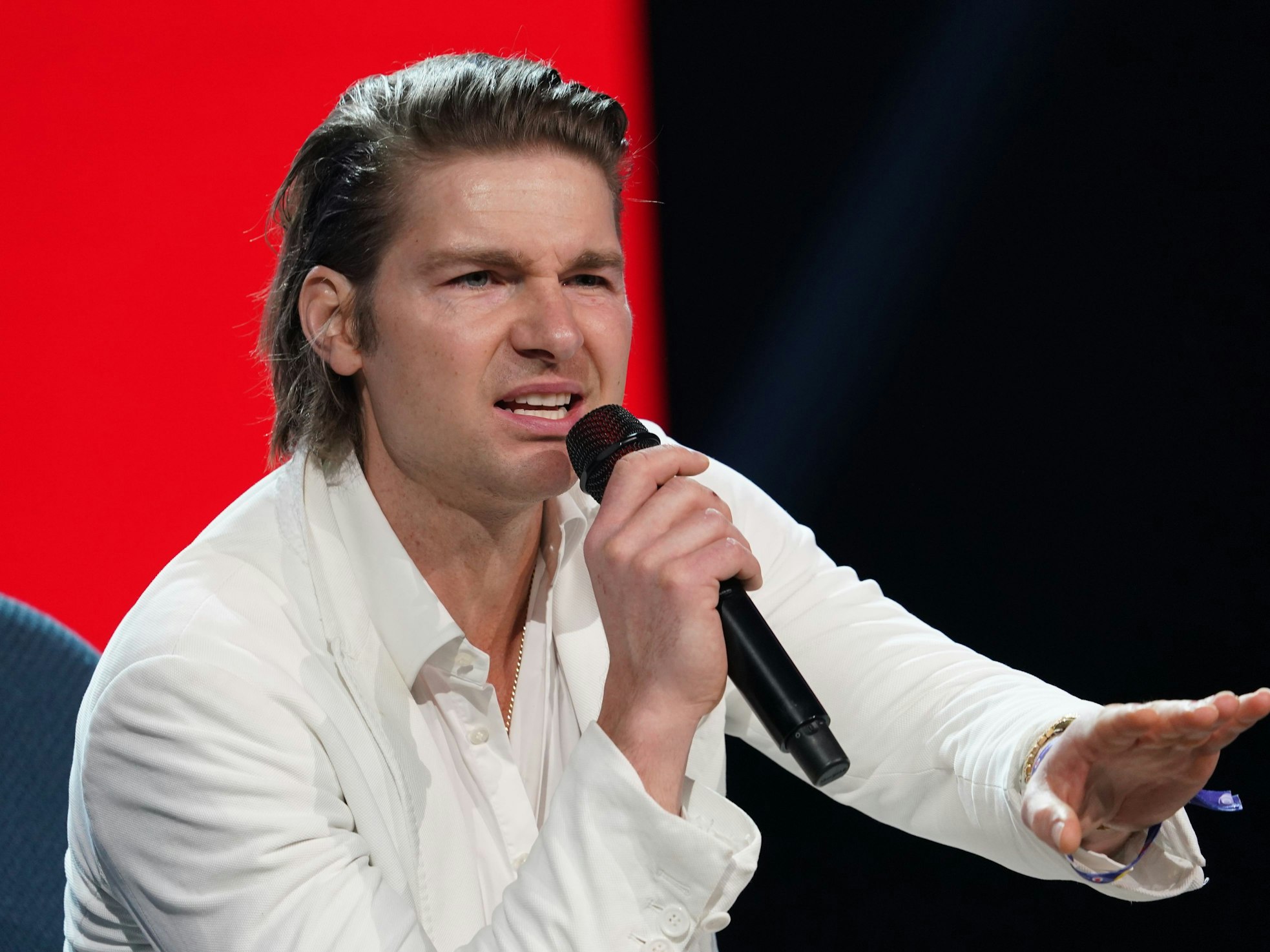 Jeremy Fragrance sitzt auf einer Bühne und spricht in ein Mikro.