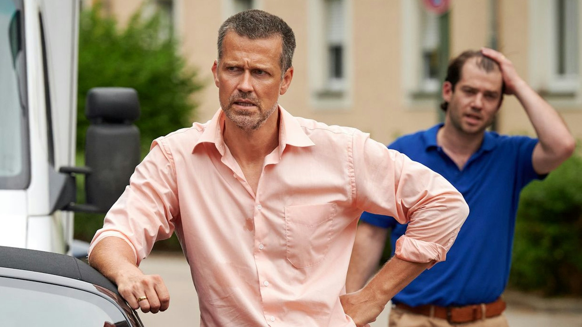 Gefangen im Stau: Familienvater Thomas Kling, gespielt von Wayne Carpendale, steht im lachsfarbenen Hemd mit düsterer Miene an ein Auto gelehnt und scheint sich zu ärgern. Das Foto aus der ZDF-Serie "Aufgestaut" ist nicht weiter datiert.