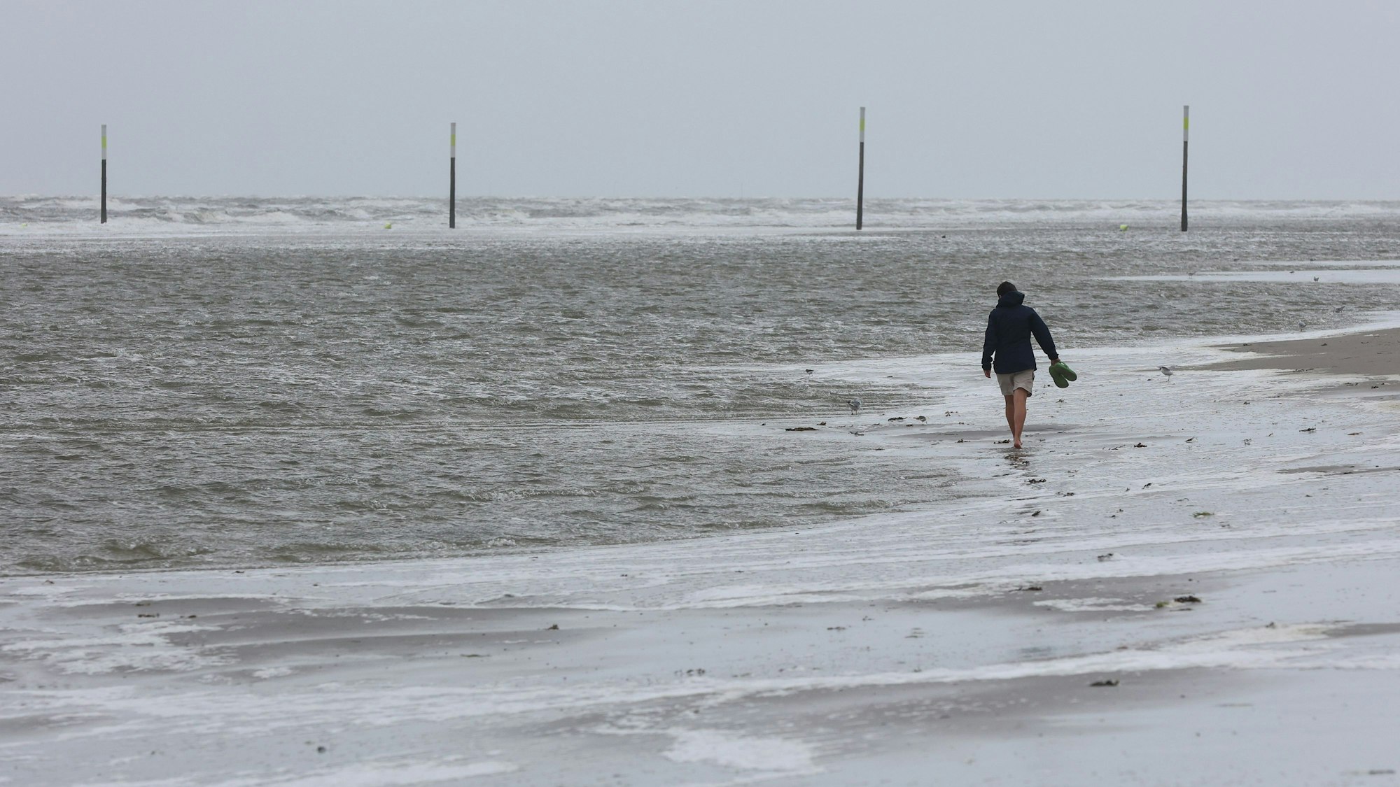 Eine Frau geht bei stürmischem Wetter am Strand spazieren.