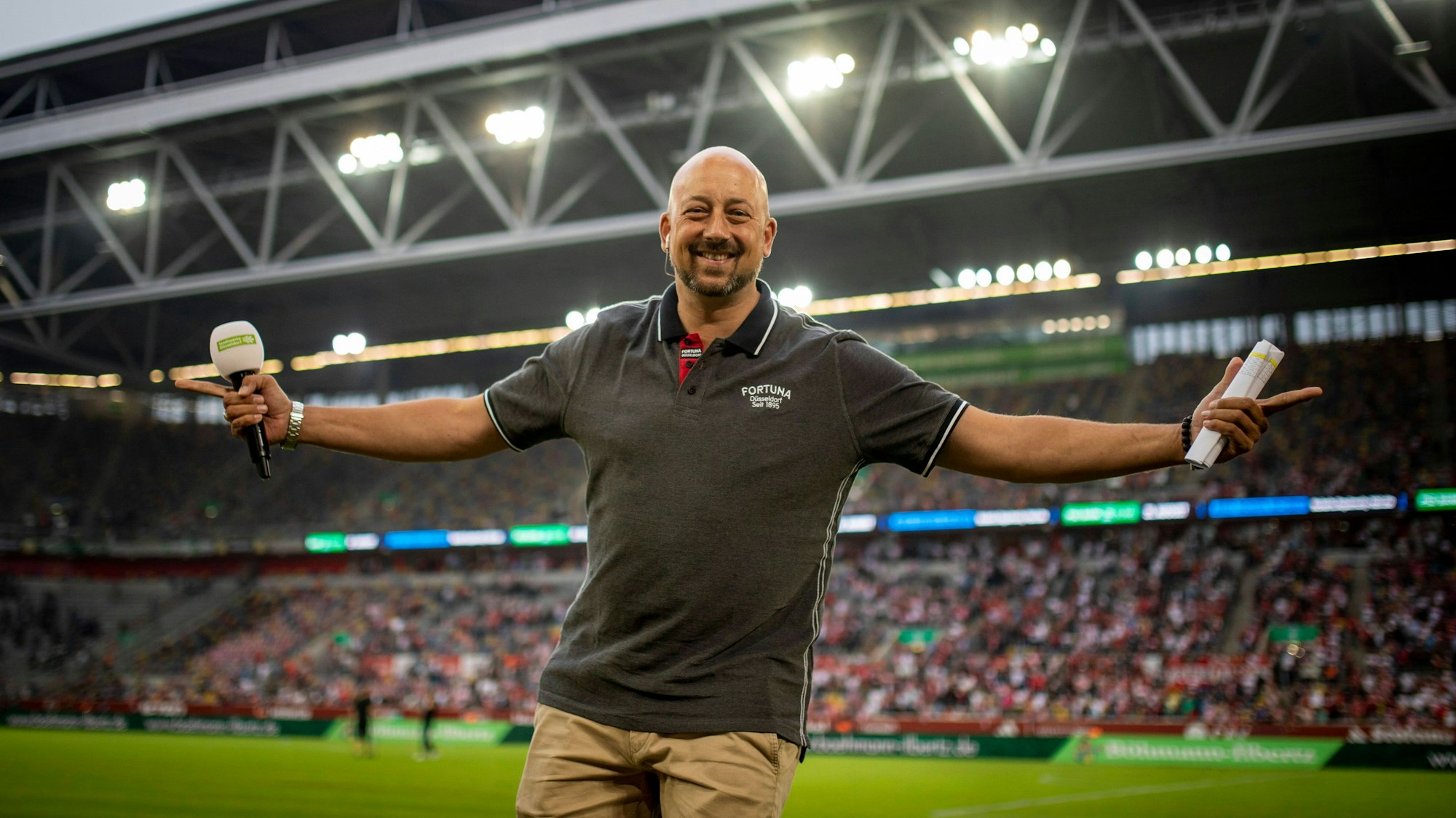 Fortuna Düsseldorfs Stadionsprecher André Scheidt lacht beim Spiel gegen den SC Paderborn in die Kamera.