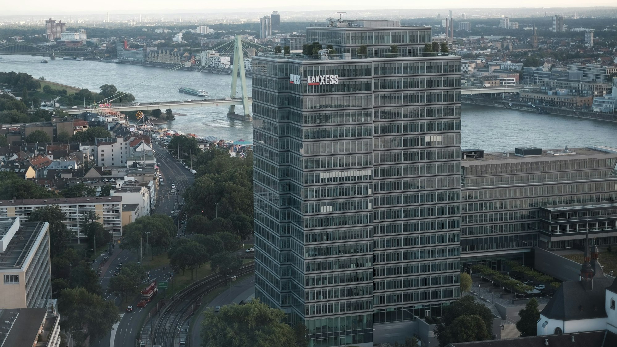 Luftaufnahme, die den Verwaltungssitz von Lanxess in Köln-Deutz zeigt. Im Hintergrund sind der Rhein und mehrere Kölner Brücken zu sehen.
