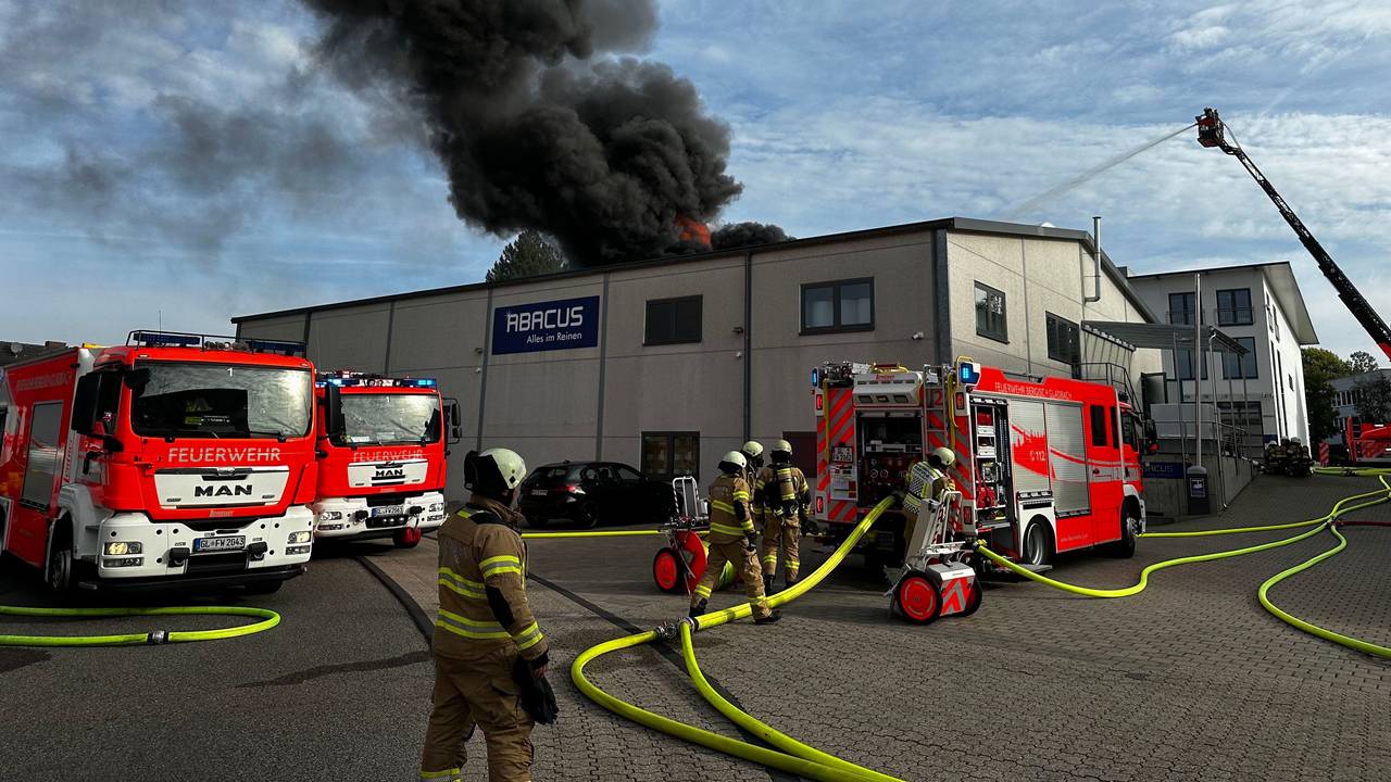 Rauch steigt über einer Lagerhalle auf, davor stehen mehrere Fahrzeuge der Feuerwehr.