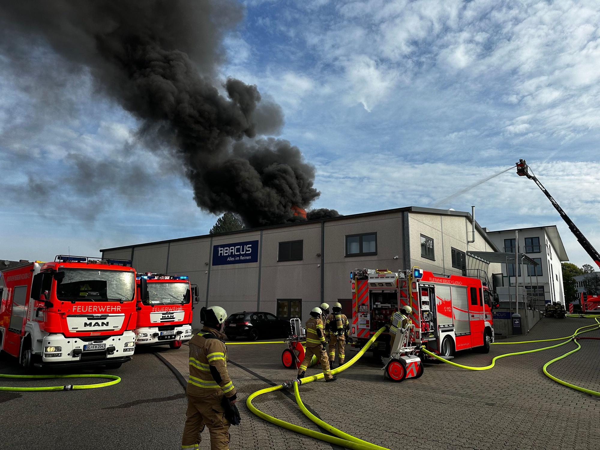 Rauch steigt über einer Lagerhalle auf, davor stehen mehrere Fahrzeuge der Feuerwehr.