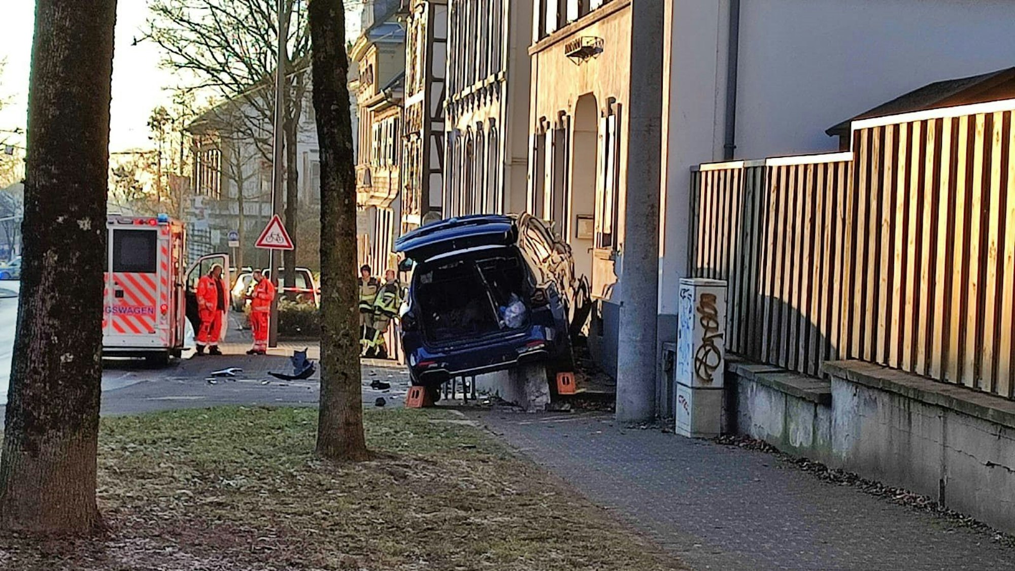 Auto steht nach einem Unfall an einer Hauswand. Im Hintergrund ist ein Krankenwagen samt Besatzung zu sehen.