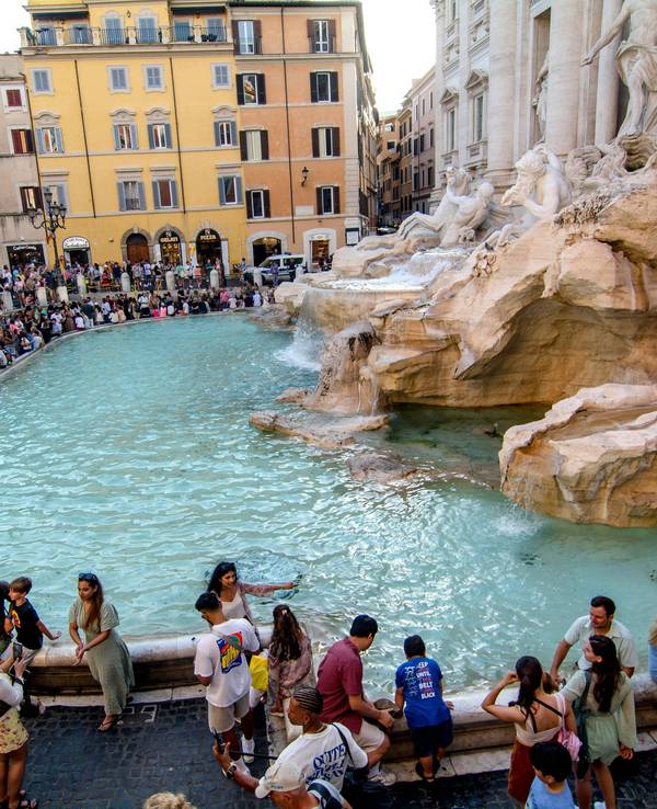 Hunderte Touristinnen und Touristen drängen sich am Rand eines Brunnens mit Säulen und Figuren.