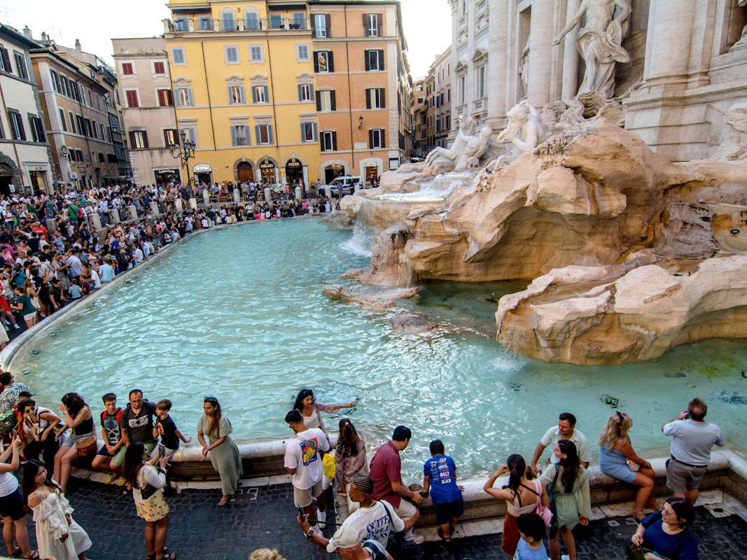 Hunderte Touristinnen und Touristen drängen sich am Rand eines Brunnens mit Säulen und Figuren.