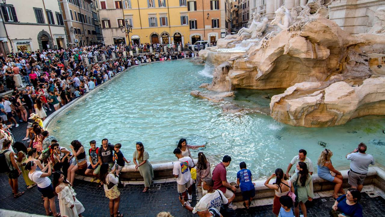 Hunderte Touristinnen und Touristen drängen sich am Rand eines Brunnens mit Säulen und Figuren.