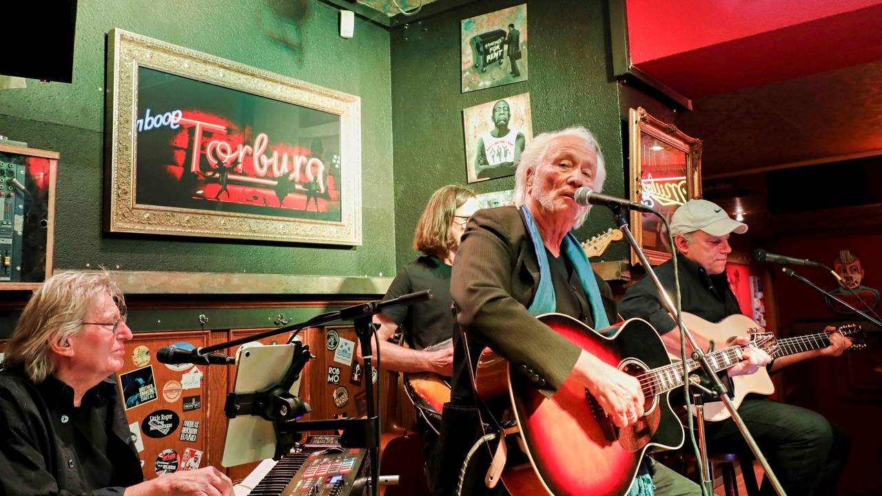 Vier Musiker mit Gitarren und Keyboard auf einer kleinen Bühne in einer Bar.
