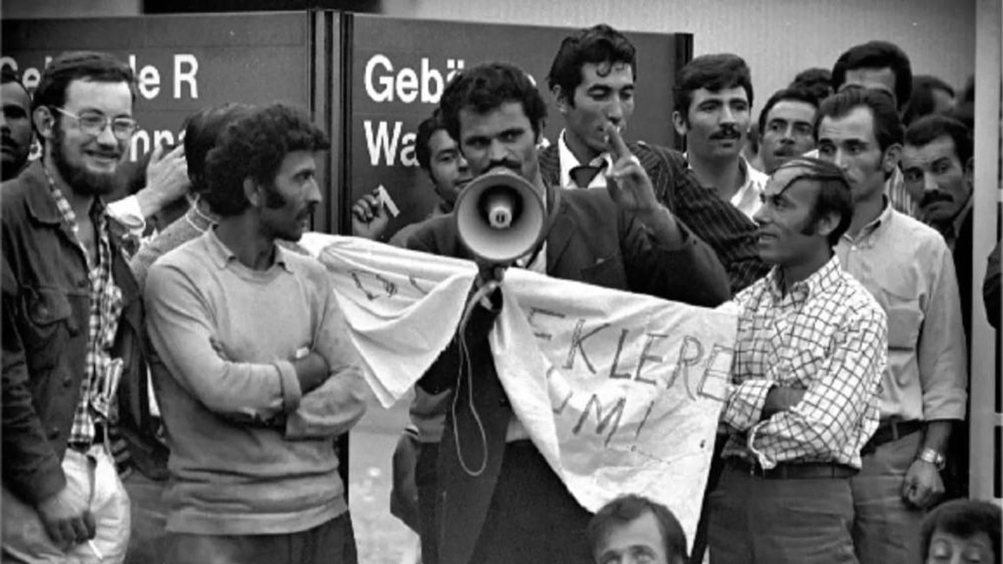 Seyfo Kurt steht mit Megafon zwischen einigen Ford-Mitarbeitern und spricht während eines Streiks im Betrieb.