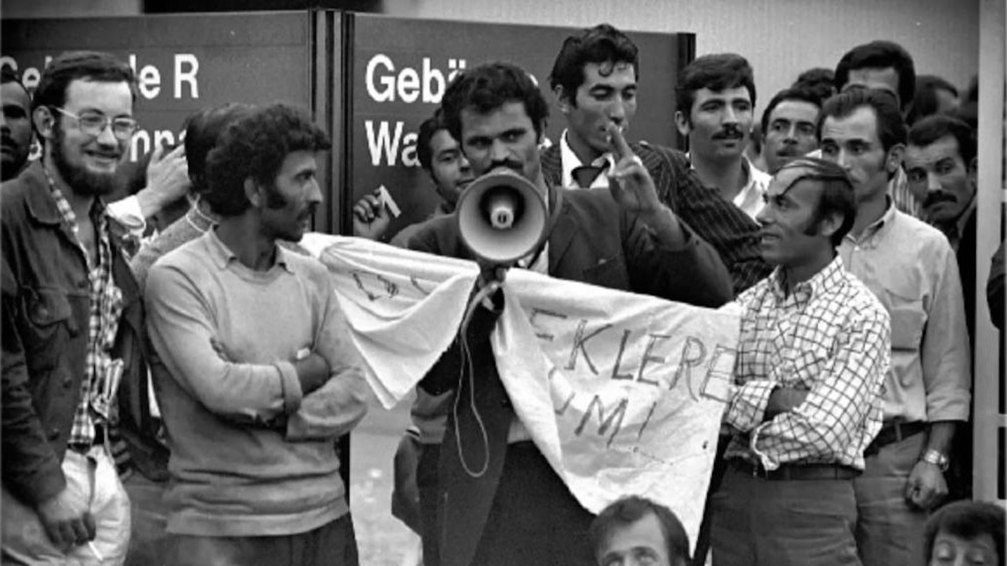 Seyfo Kurt steht mit Megafon zwischen einigen Ford-Mitarbeitern und spricht während eines Streiks im Betrieb.