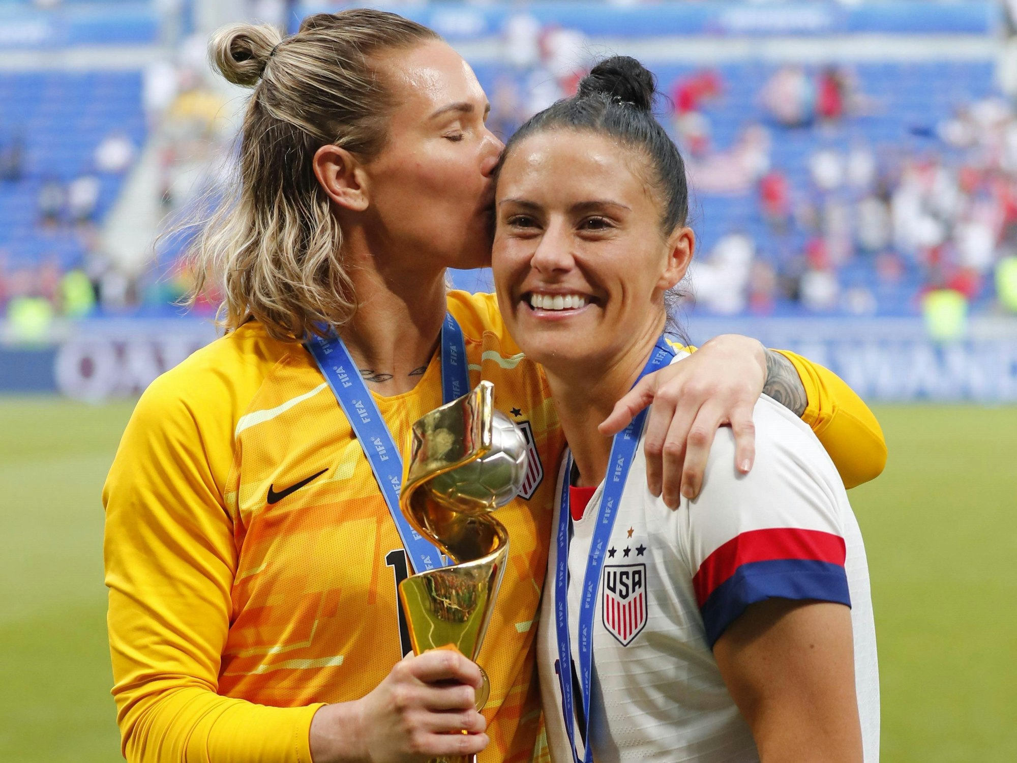 Ashlyn Harris küsst Ali Krieger nach dem WM-Finale 2019 auf die Schläge, sie hält den WM-Pokal in der Hand.