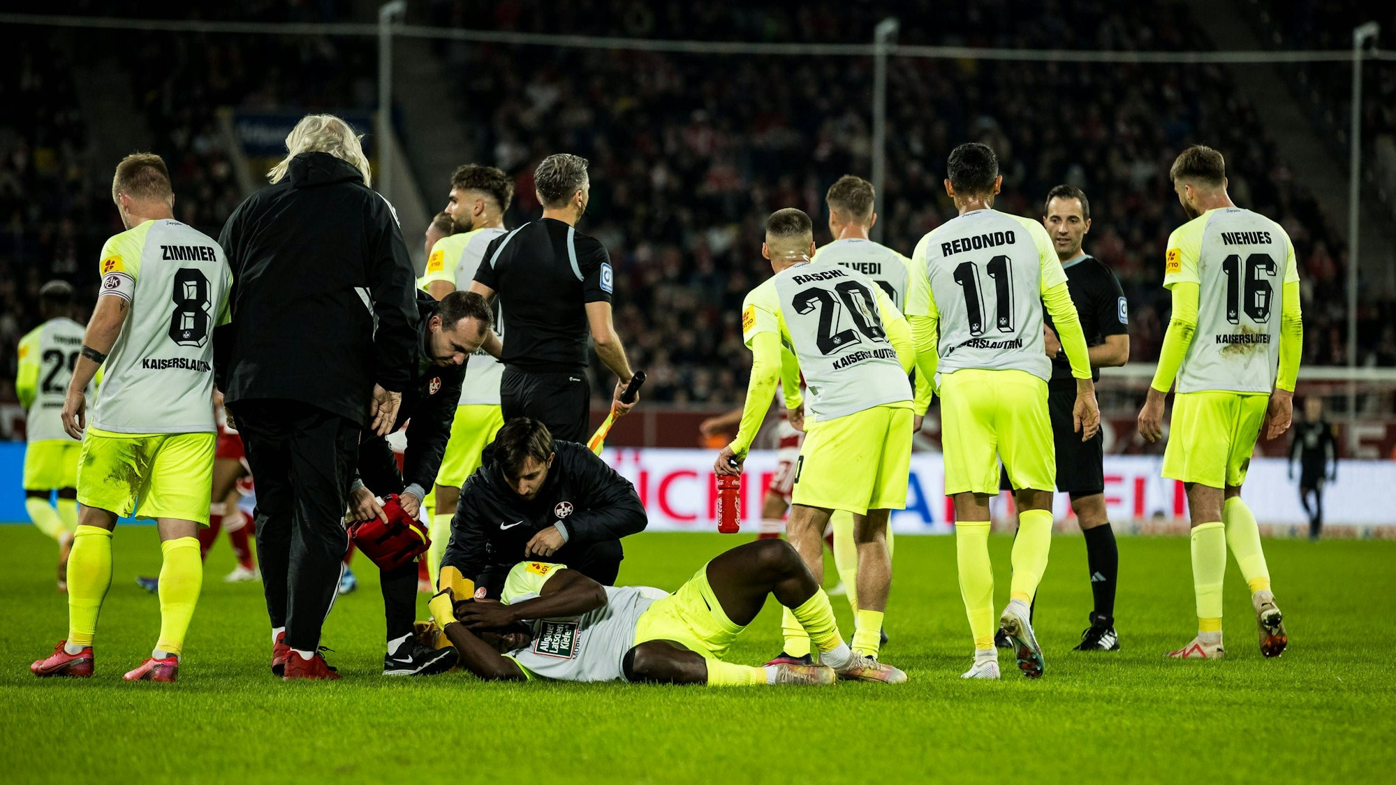 Kaiserslauterns Ragnar Ache liegt am Boden, um ihn herum stehen seine Teamkollegen.