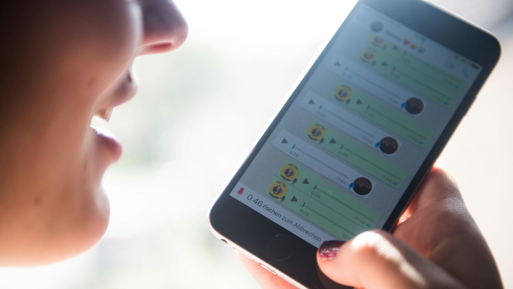 Eine Frau hält sich das Handy vor dem Mund und nimmt eine Sprachnachricht auf.