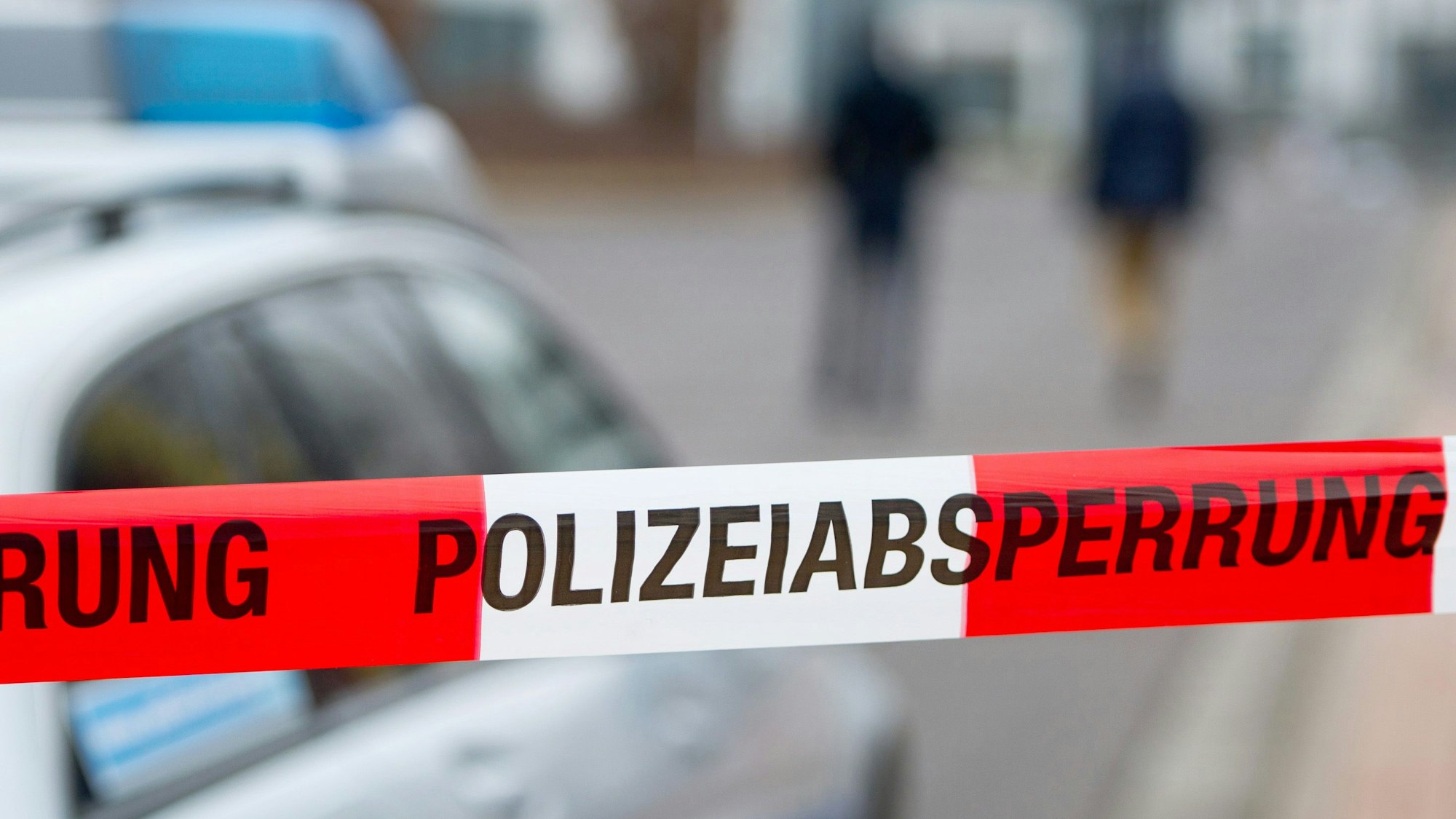 Ein Polizeiabsperrband ist vor einem Polizeiwagen zu sehen.