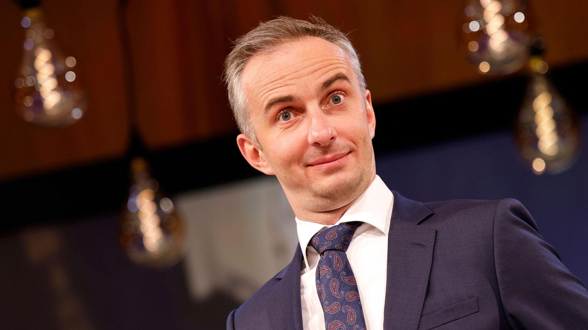 Jan Böhmermann im Anzug, er zieht die Augenbrauen hoch und lächelt leicht.