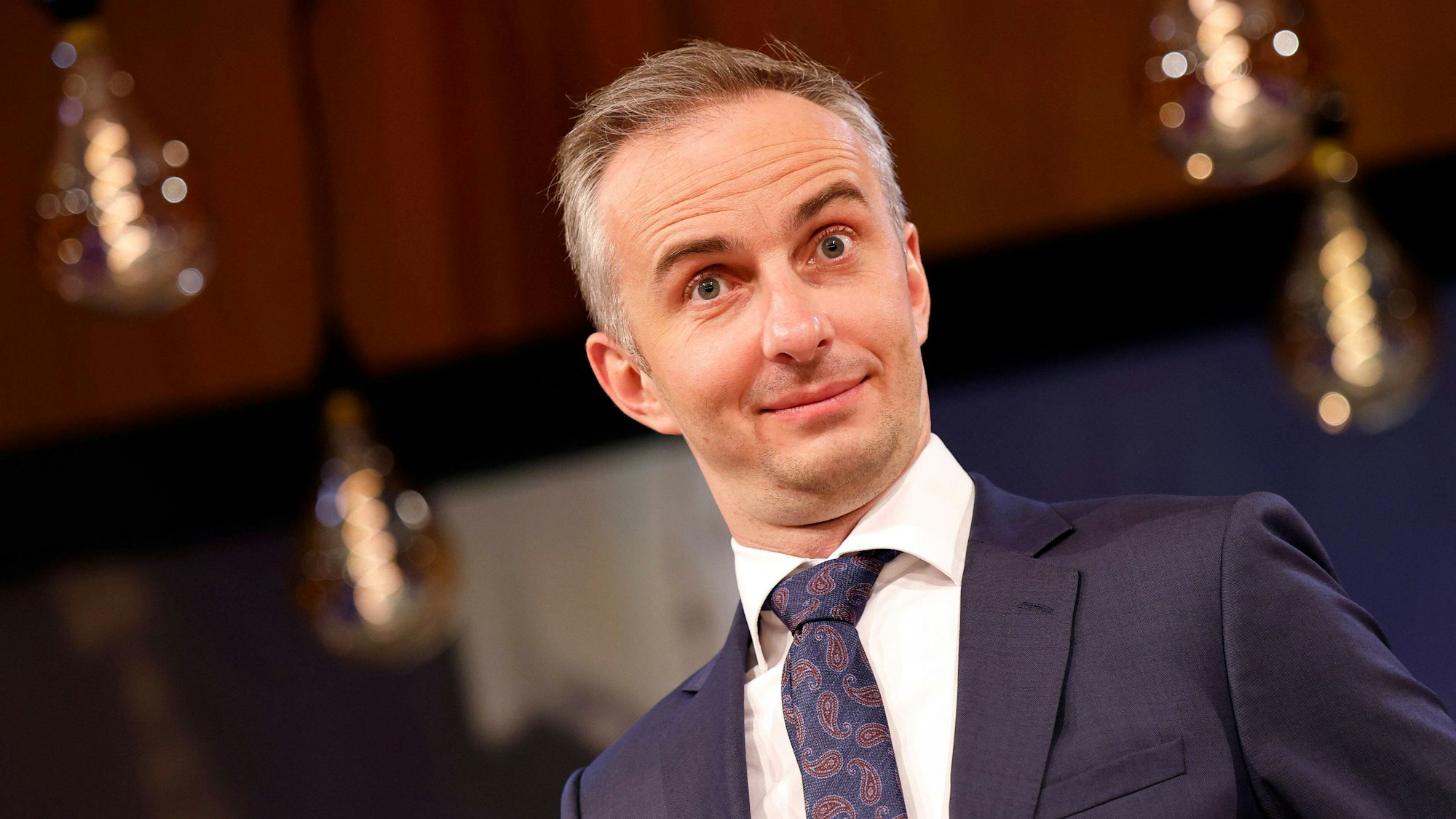 Jan Böhmermann im Anzug, er zieht die Augenbrauen hoch und lächelt leicht.