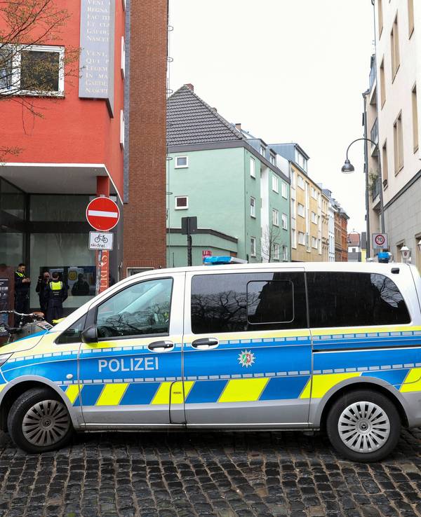 Polizei-Auto steht an einer Straße in Köln, im Hintergrund sind mehrere Einsatzkräfte und Privatpersonen zu sehen.