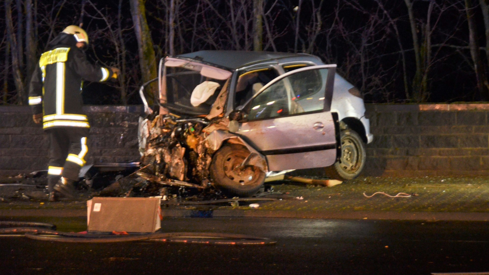 Ein Unfallauto steht in Köln-Niehl und wird von einem Feuerwehrmann begutachtet.