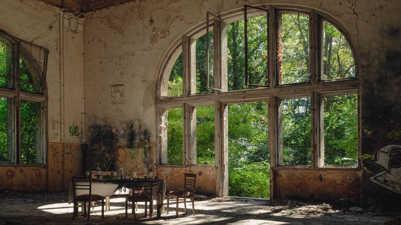 Symbolbild Beelitz Heilstätten Deutschland, Beelitz am 09.09.2023: In der Ruine des Speisesaals im Alpen-Haus stehen fünf alte Stühle und um einen alten Tisch mit Gläsern und eine Flasche vor einem riesigen Fenster.