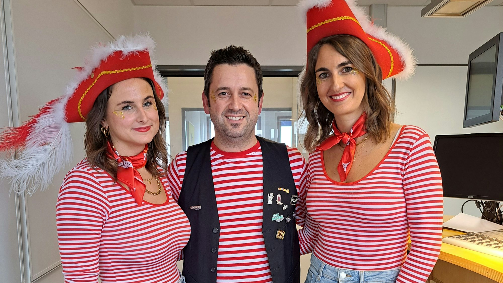 Zwei Frauen und ein Mann in einem Tonstudio, sie lächeln in die Kamera.