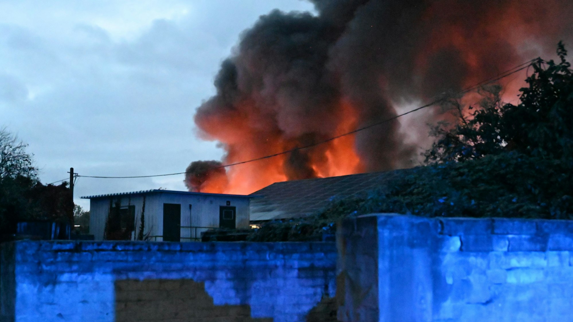 Ein großes Feuer in einer Lagerhalle in Frechen, im Hintergrund sind dunkle Rauchwolken zu sehen.