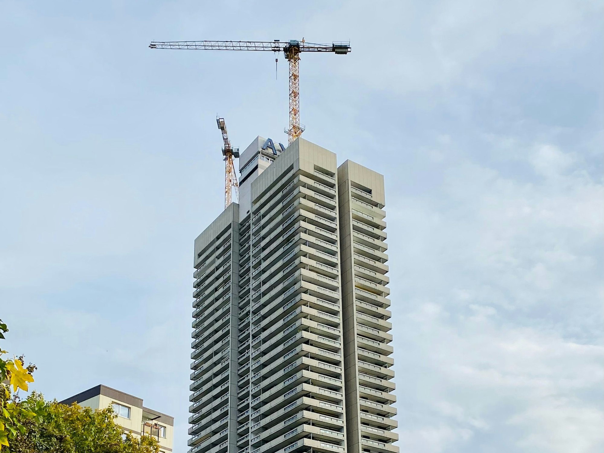 Blick aus der Ferne auf das Colonia-Haus in Köln, auf dem Kräne angebracht sind.