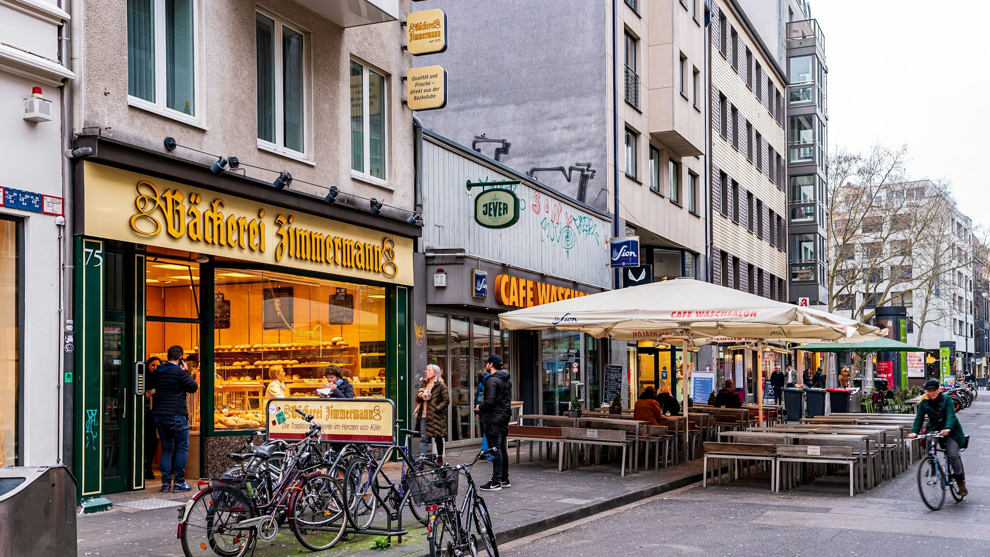 Foto von der Kölner Ehrenstraße. Unter anderem sind die Bäckerei Zimmermann und das Café Waschsalon zu sehen.