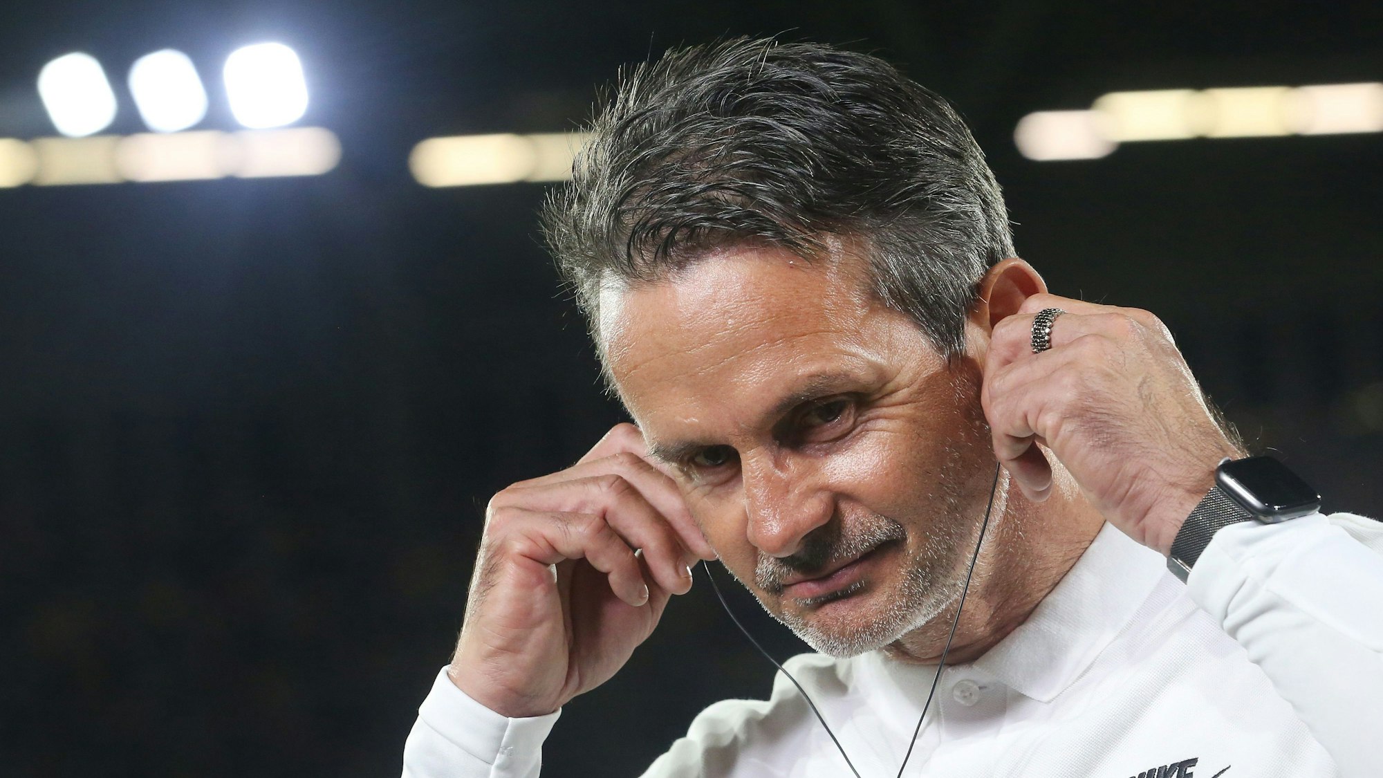 Dirk Schuster steckt sich für ein TV-Interview Kopfhörer in die Ohren.