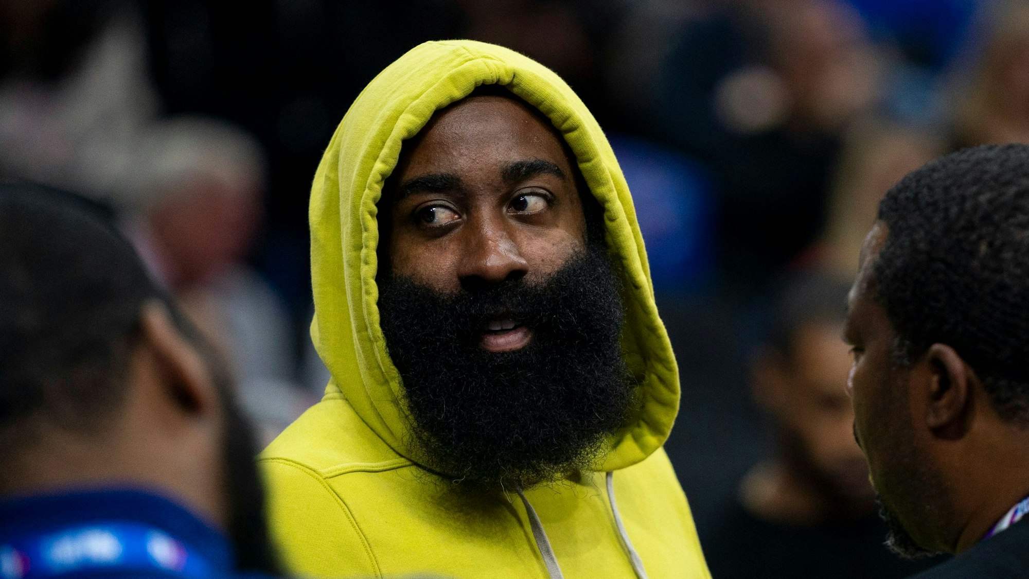 James Harden guckt sich das Spiel der 76ers gegen die Portland Trail Blazers als Zuschauer an. Er trägt einen gelben Hoodie und hat die Kapuze über den Kopf gezogen.
