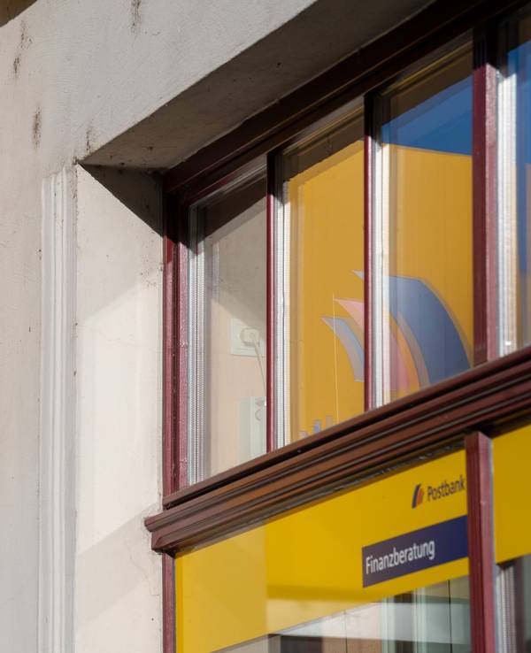 Ein gelbes Postbank-Schild ist an einem grauen Gebäude befestigt.