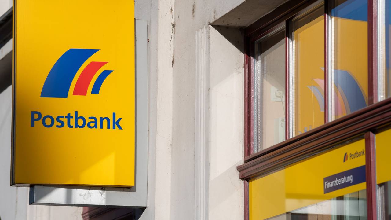 Ein gelbes Postbank-Schild ist an einem grauen Gebäude befestigt.