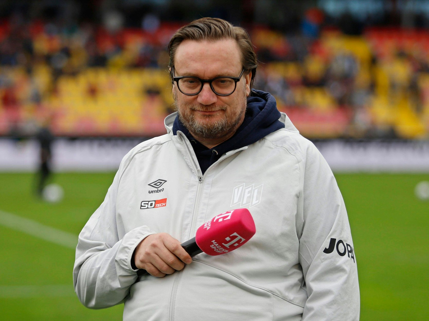 Michael Welling am Rand eines Fußballfelds mit Mikrofon.