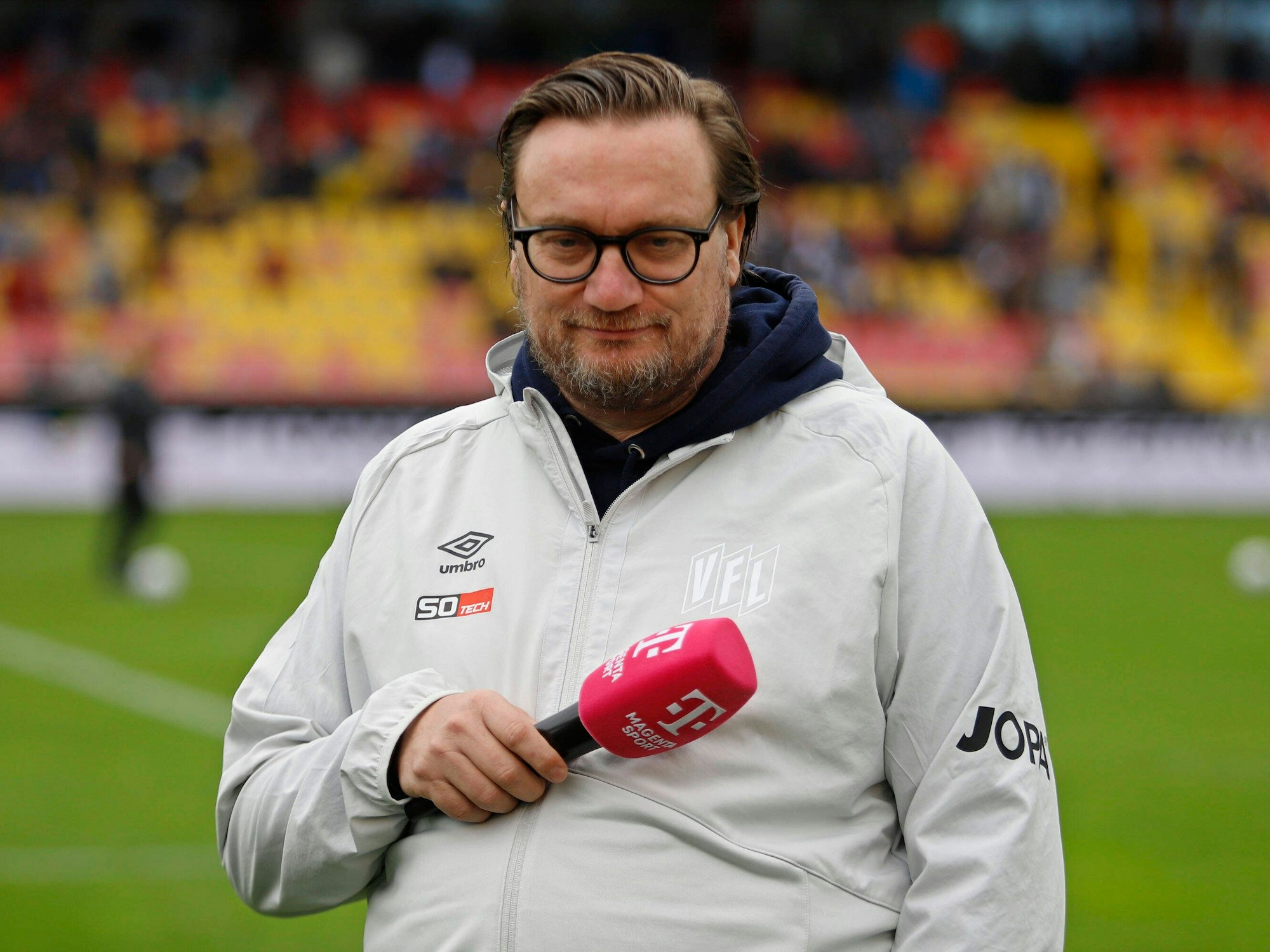 Michael Welling am Rand eines Fußballfelds mit Mikrofon.