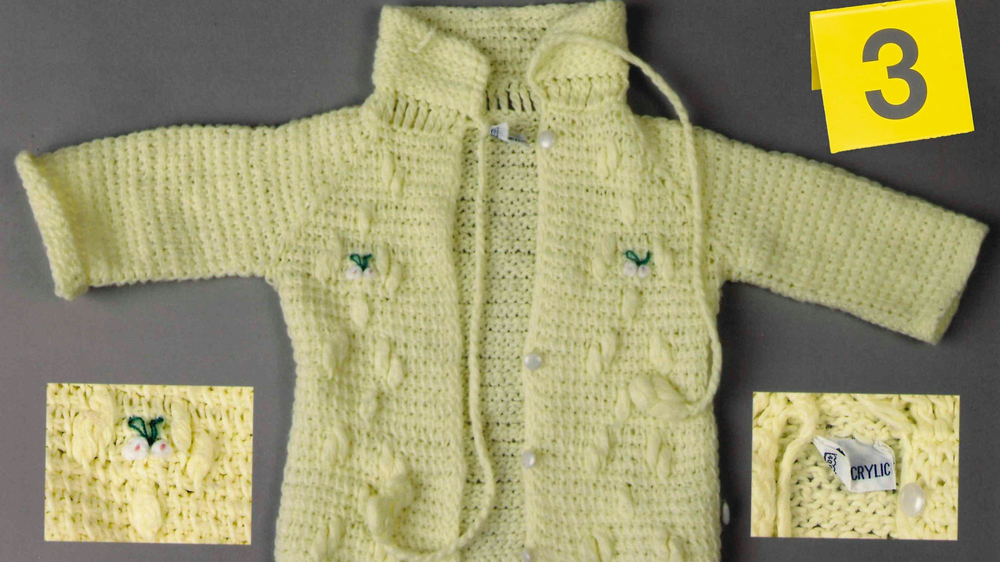 Ein gelbes Babyjäckchen liegt auf einem Tisch. +