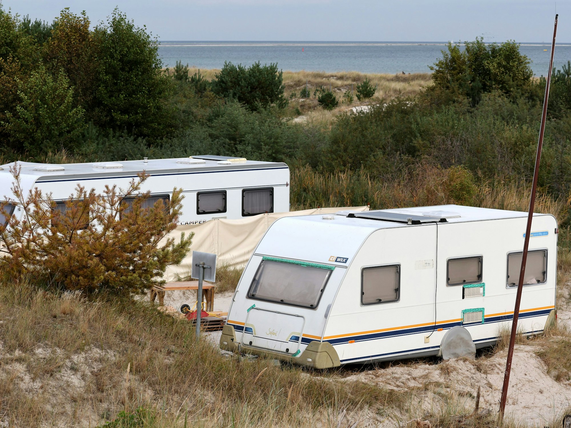 Zwei Wohnwagen stehen im Sand in Meernähe.