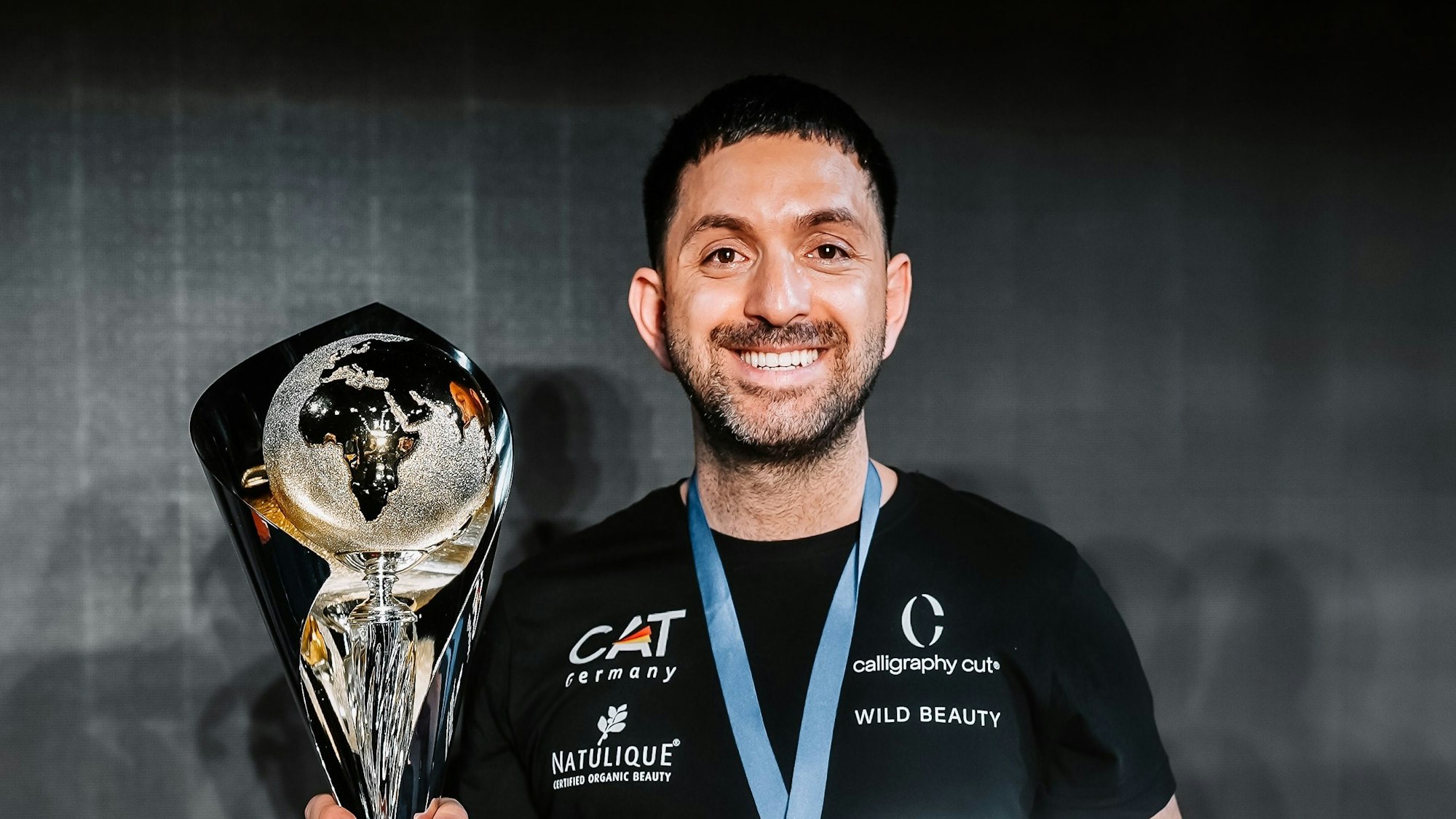 Der Düsseldorfer Friseur Melih Benderlioglu posiert in Neapel mit dem Weltmeister-Pokal im Team-Wettbewerb Damen-Fach.