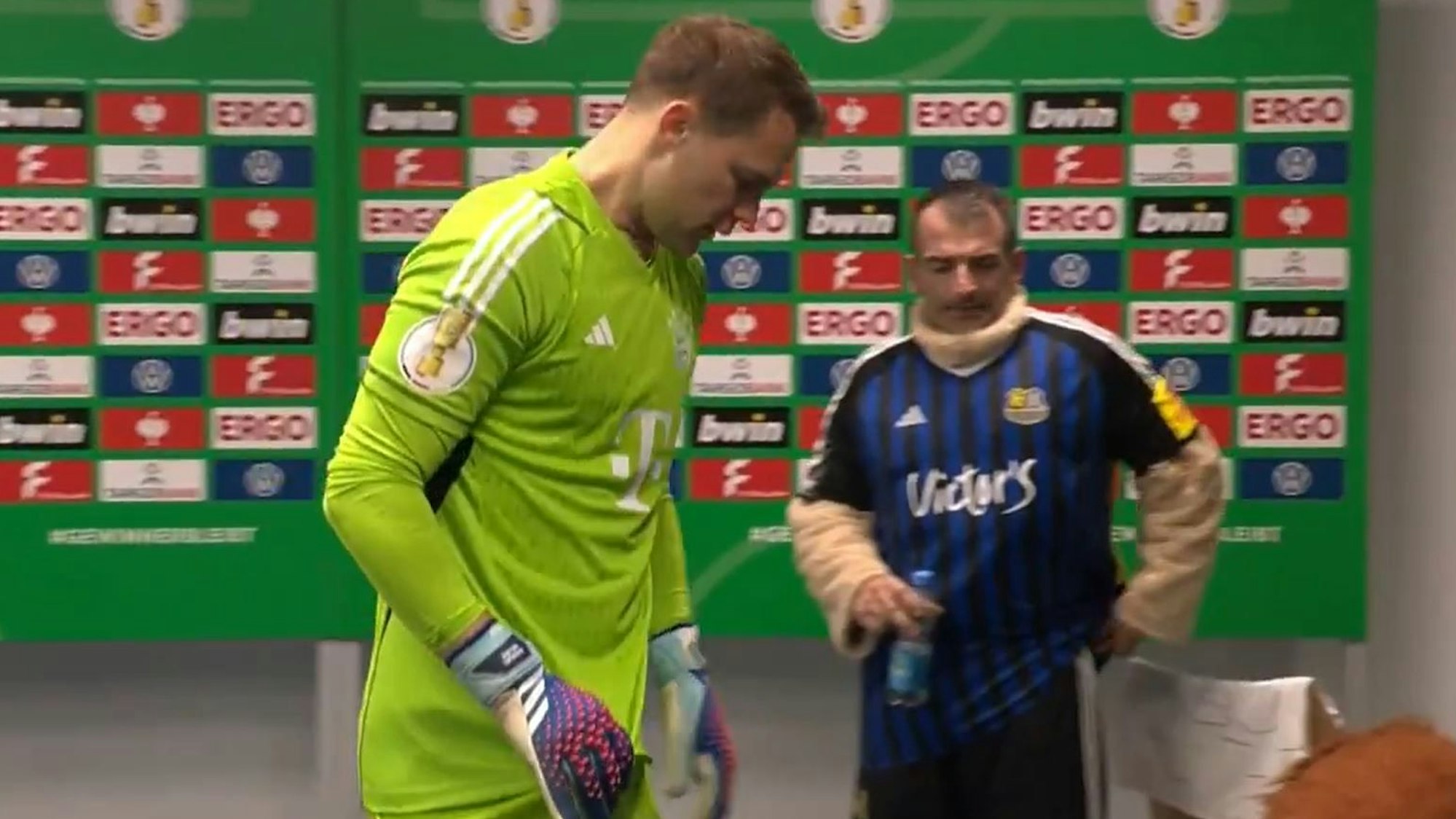 Hinter Manuel Neuer ist beim Spiel im DFB-Pokal zwischen dem 1. FC Saarbrücken und dem FC Bayern München das Maskottchen der Gastgeber ohne seinen Löwenkopf zu sehen.