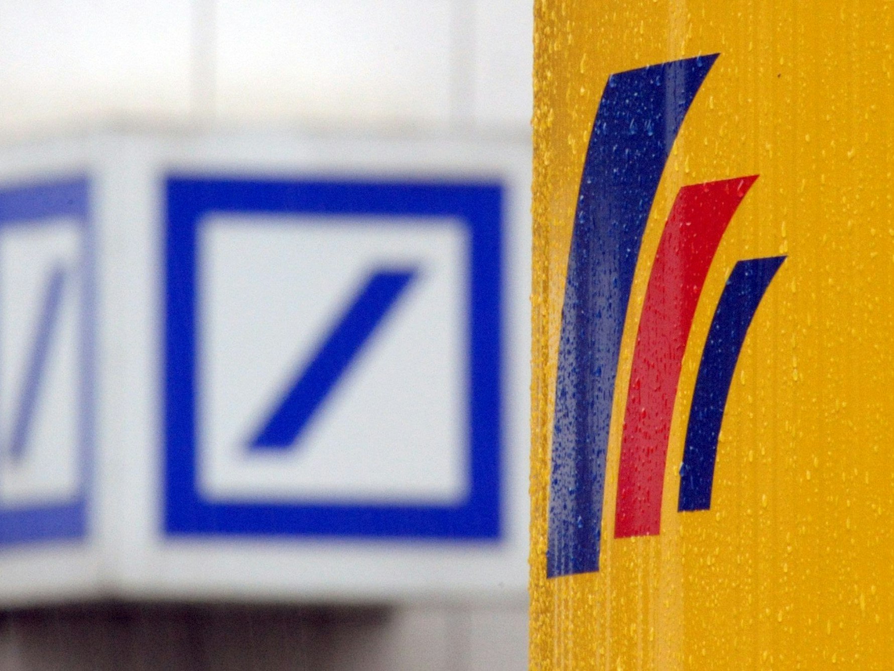 Das Logo einer Filiale der Deutschen Bank (l) und das Logo der auf der gegenüberliegenden Straßenseite befindlichen Postbank-Zentrale in Bonn.